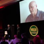 Ken Newton (left) at the Wire & Gas 2022 VASA Pioneer Award ceremony playing a video interview he did with Rick Pickering